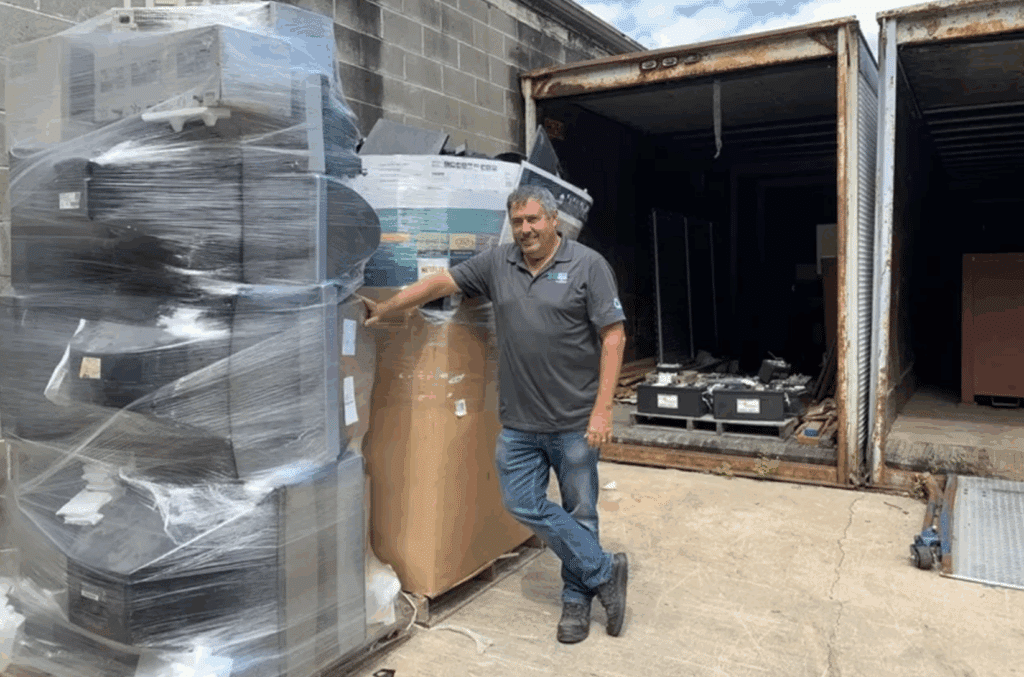 A man standing next to a large pile of electronics for recycling